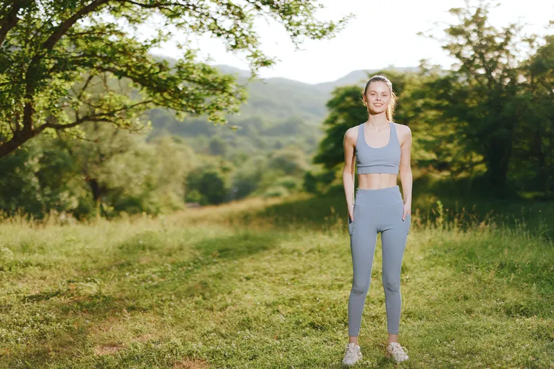 Young woman in activewear smiling outdoors, showcasing fitness and well being in a serene natural setting, ideal for health and wellness themes