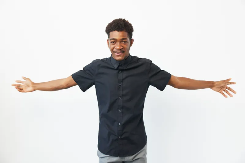 A cheerful black man expressing joy with open arms, wearing a stylish black shirt against a plain white background, creating an uplifting and vibrant atmosphere.