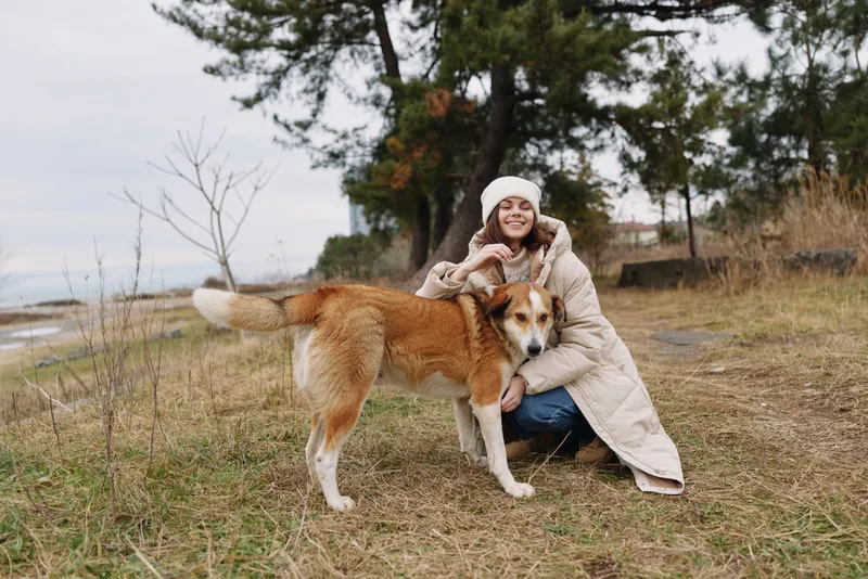 Woman, dog, outdoors, companionship, coat, fall scene with a smiling pair enjoying a chilly park moment.