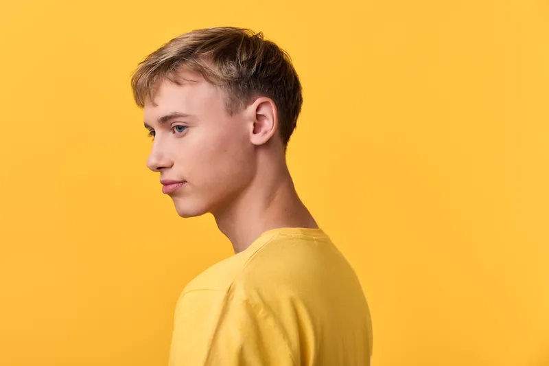 Side profile of a young man in a yellow shirt against a solid yellow background, calm expression, clean studio shot with minimal styling for fashion, lifestyle or advertising campaigns