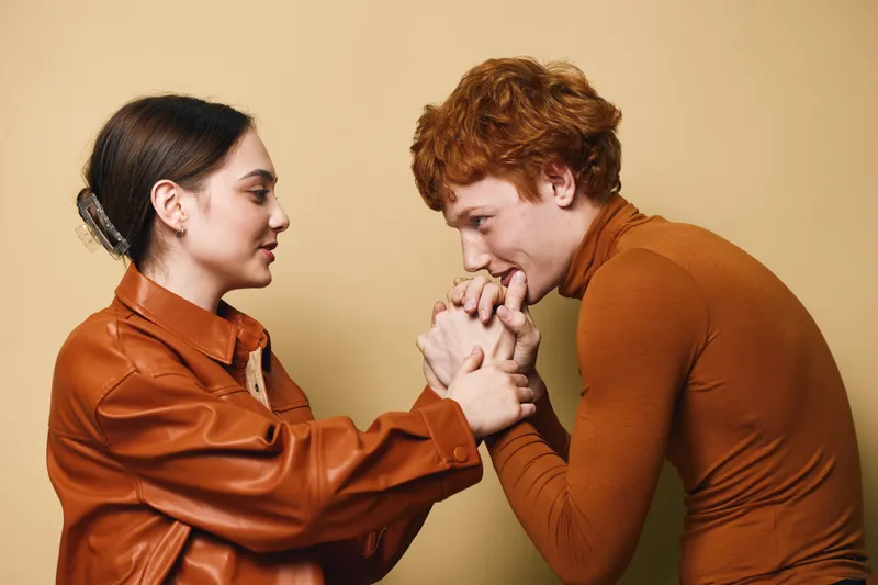 Couple in warm clothes showing affection and tenderness with intimate gesture on plain background. Young man and woman expressing care and connection.
