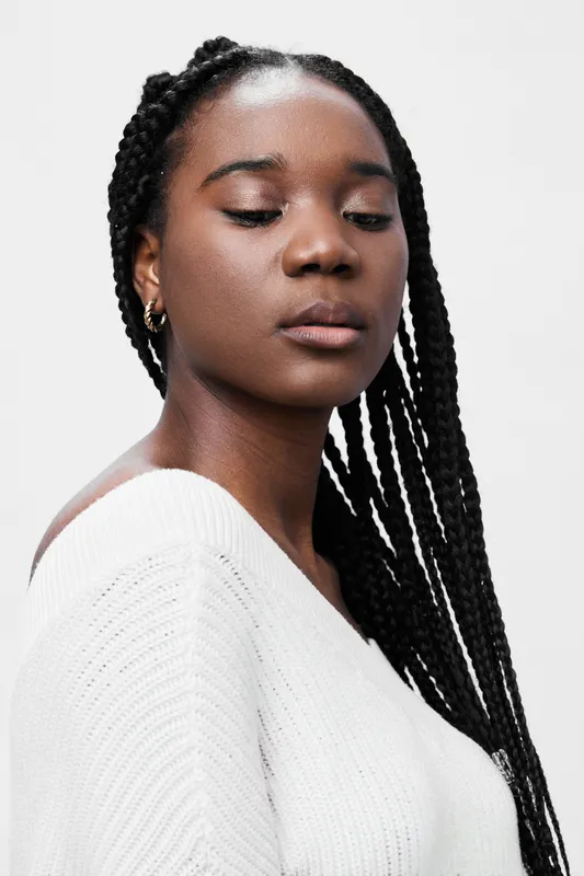 Portrait of a confident Black woman with braids, wearing a white sweater, exuding elegance and serenity against a simple white background, ideal for beauty and fashion concepts