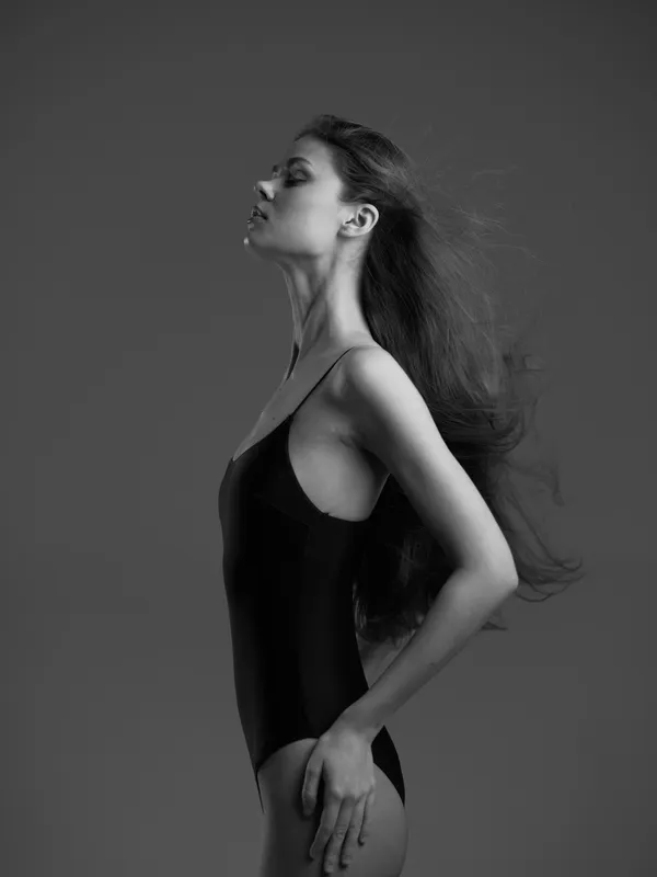 Black and white portrait of a calm woman with long hair posing in a leotard on a gray background