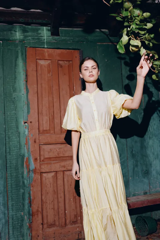 Woman portrait in yellow dress by door with sunlight, authentic inclusive summer mood