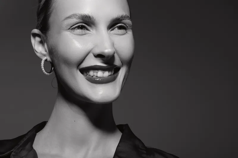 Smiling Caucasian woman with light skin and short hair wearing hoop earrings. Close-up portrait in black and white with bright studio lighting. Concept of happiness and beauty.