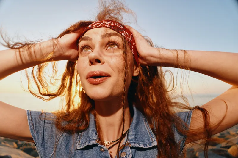 Lifestyle woman in modern boho-western denim street style looks upward with dreamy expression, film color tones enhancing natural sunlight and relaxed summer vibe.