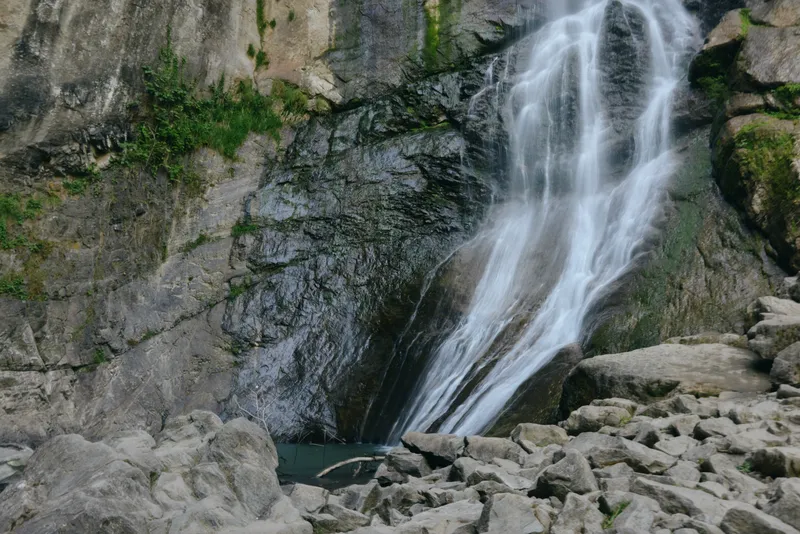 waterfall cascading down rocky cliff surrounded by green moss and scattered stones, natural flowing water and serene outdoor landscape