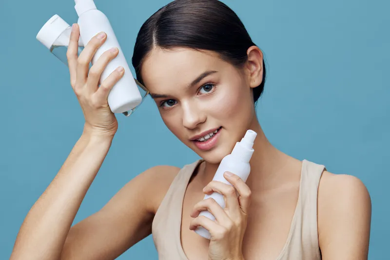 Young woman with beautiful skin holding skincare products, showcasing a healthy lifestyle and skincare routine against a soft blue background