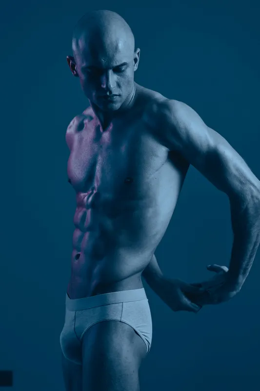 Muscular man posing in a dramatic blue lighting, showcasing strength and confidence in a stylish and artistic manner, perfect for fitness and wellness themes.