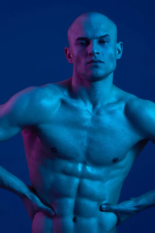 Muscular man with bold expression showcasing strength and intensity under vibrant blue and pink lights. Evoking a sense of power and emotion in a striking visual.