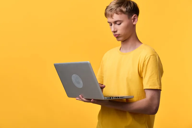 Man in a yellow shirt using a laptop against a bright yellow background, focusing on digital work, learning and online collaboration, modern tech setup in a minimal studio style