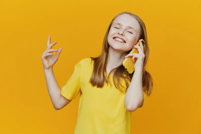 Happy young girl in yellow t shirt smiling while talking on the phone against a bright yellow background, conveying joy and positivity