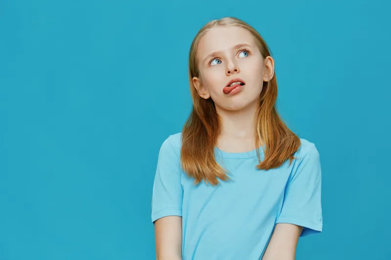 Playful girl sticking out her tongue in a blue t shirt against a bright blue background, showcasing youthfulness and fun emotions in a vibrant setting