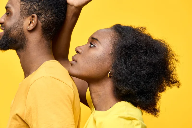 Young Black couple with natural hairstyles against a vibrant yellow background, showcasing love and togetherness in a stylish and refreshing manner