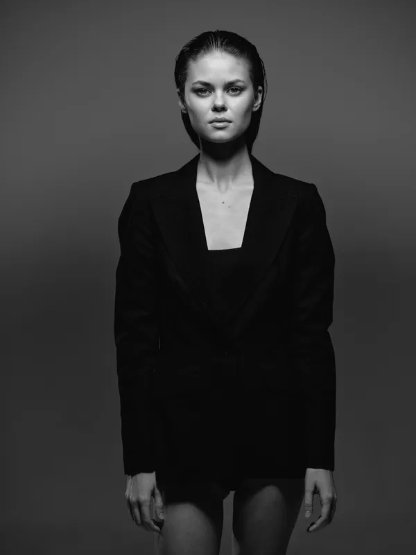 Black and white portrait of a serious woman in a dark blazer with wet hair, minimalist style, studio lighting, emotional expression