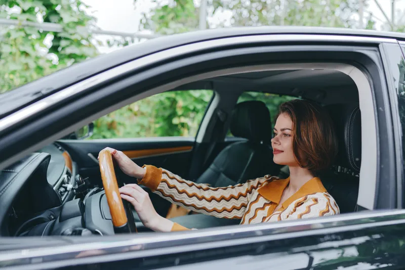 Female driver sits behind the wheel in a modern car, focused on the road, steady hands on the steering wheel, calm and confident.