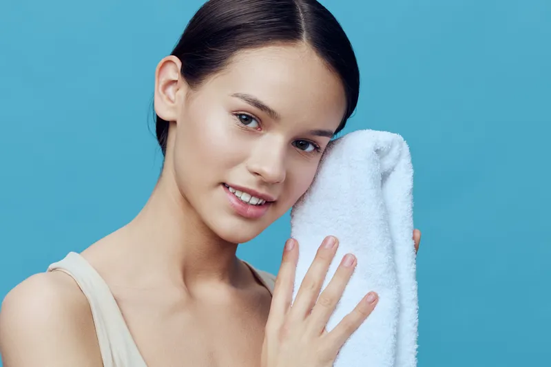 Young woman with towel on blue background, showcasing healthy skin and natural beauty, smiling with confidence and warmth in a skincare concept