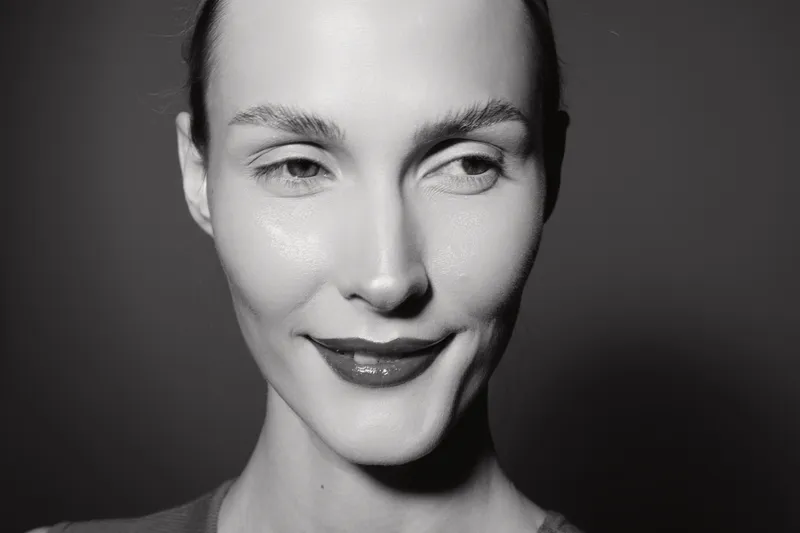 Close-up portrait of a young white woman with pale skin smiling softly. Black and white studio photo emphasizing natural beauty and subtle positive emotion in monochrome.