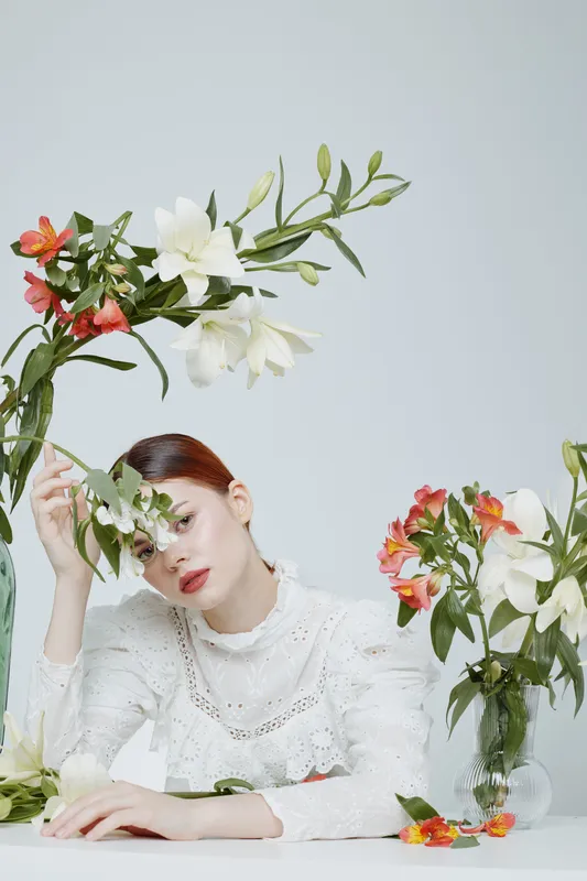 A serene young woman of Asian descent in a white lace blouse surrounded by colorful floral arrangements, conveying feelings of tranquility and beauty in spring