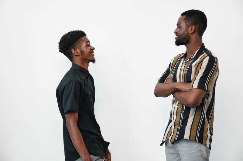 Two African American men with dark skin standing and smiling at each other in casual clothes on white background. Friendship, communication and positive interaction.