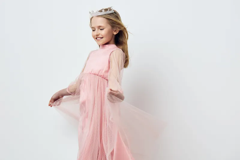 A joyful young girl in a flowing pink dress twirls gracefully, showcasing her playful spirit and innocence in a minimalist studio setting with soft pastel tones