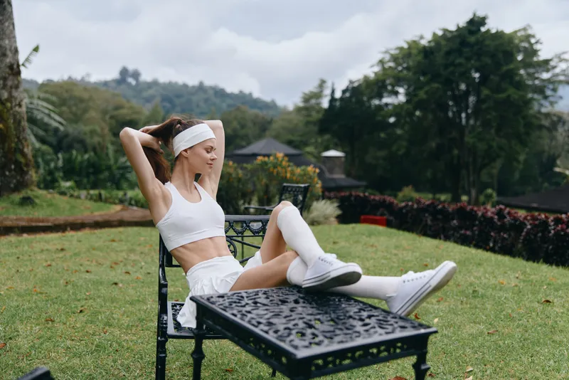 Young athletic woman relaxing outdoors in sporty white outfit, expressing calmness, surrounded by nature in a vibrant green setting