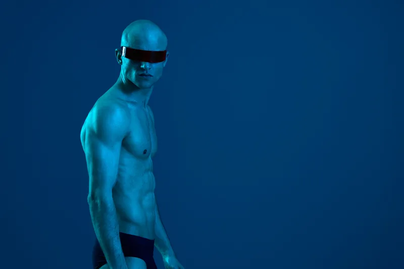 Strong man posing in a striking blue light, showcasing his physique and confidence, exuding a futuristic style that captivates attention and intrigue.
