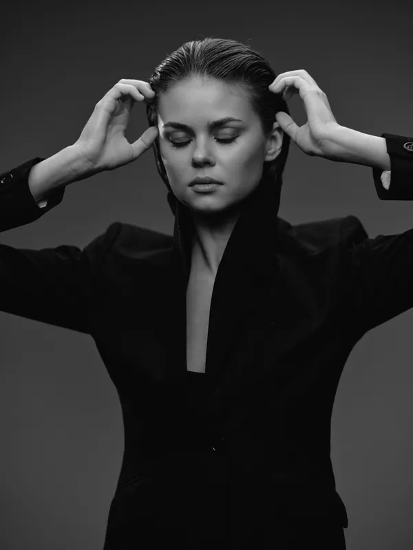 Black and white portrait of a thoughtful woman in a blazer with closed eyes and hands near her head, expressing calm and focus.