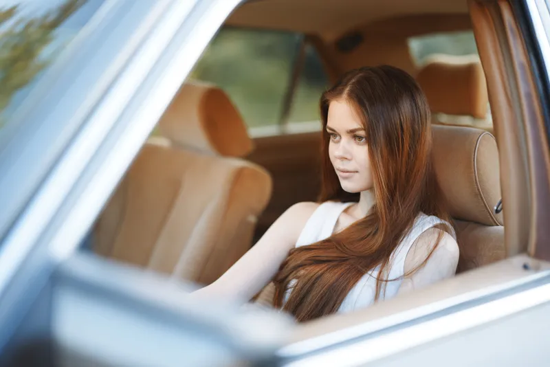 Young woman with long hair sitting in a vintage car, conveying a sense of nostalgia and tranquility in soft natural light.