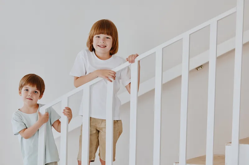 Two playful boys climbing the stairs, showcasing their joy and sibling bond in a bright, modern interior setting filled with natural light.