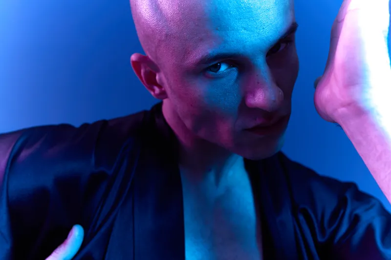 Intense man with a sleek bald head showcases bold emotions against a vibrant blue background. This striking image captures raw energy and artistic flair.