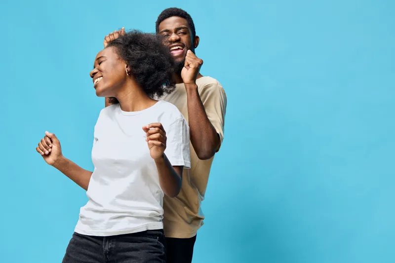 Happy young couple dancing against a vibrant blue background, showcasing joy, connection, and fun moments in casual attire to express togetherness and enjoyment