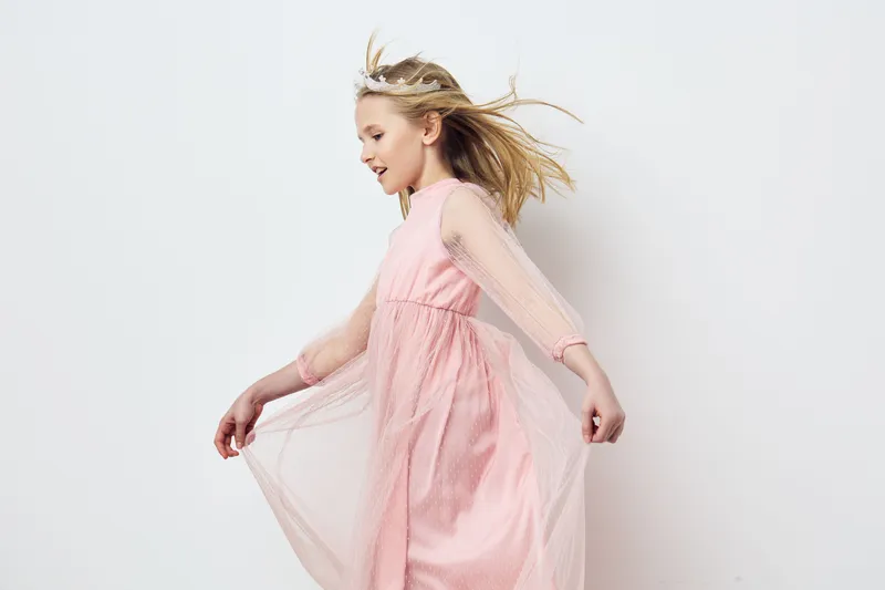 Happy girl in a flowing pink dress enjoying a playful moment, showcasing innocence and joy in a minimalistic, light background