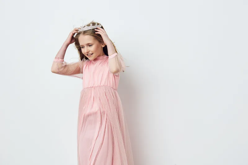 Young girl in a pink dress with a crown, joyfully playing against a soft white background, embodying innocence and happiness, perfect for seasonal celebrations