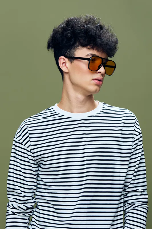 young man wearing striped shirt and orange sunglasses posing against green background with curly hair, casual style, modern fashion portrait