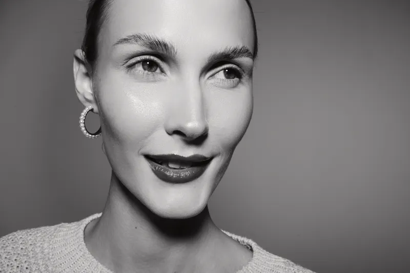 Close-up portrait of a young white woman with smooth skin and dark hair pulled back, wearing earrings and a sweater. Concept of beauty, fashion, and natural elegance in black and white.
