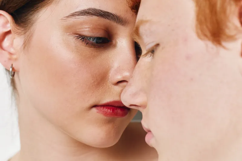 Closeup of two young adults with emotional expression sharing intimate moment, skin details and natural light highlighting facial features and connection.