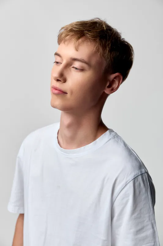 Young man, white t shirt, calm, serene, studio, minimal, relaxed, thoughtful, eyes closed, soft lighting, simple background, clean composition, fashion vibe, quiet confidence, gentle pose, everyday