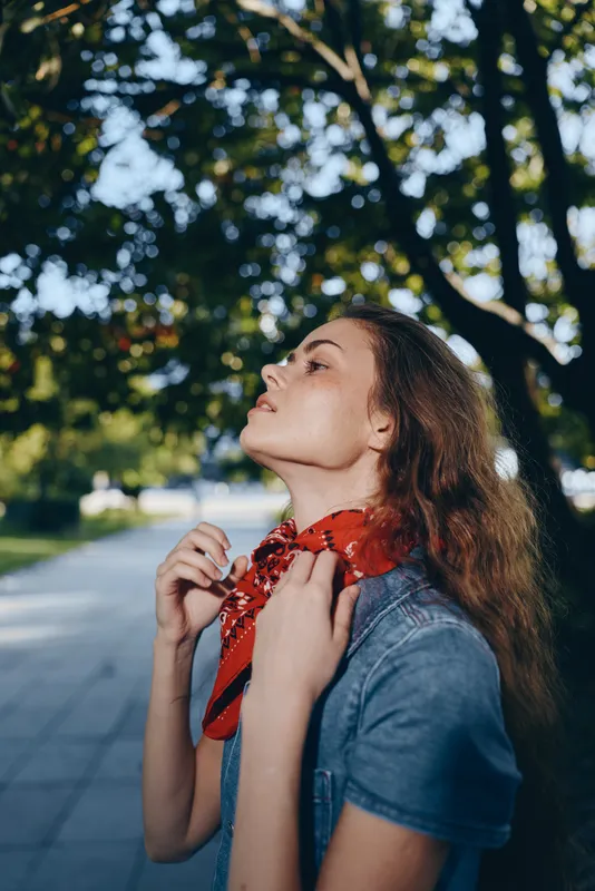 lifestyle woman in modern boho-western denim street style with red bandana, natural light, and film color tones in outdoor park setting