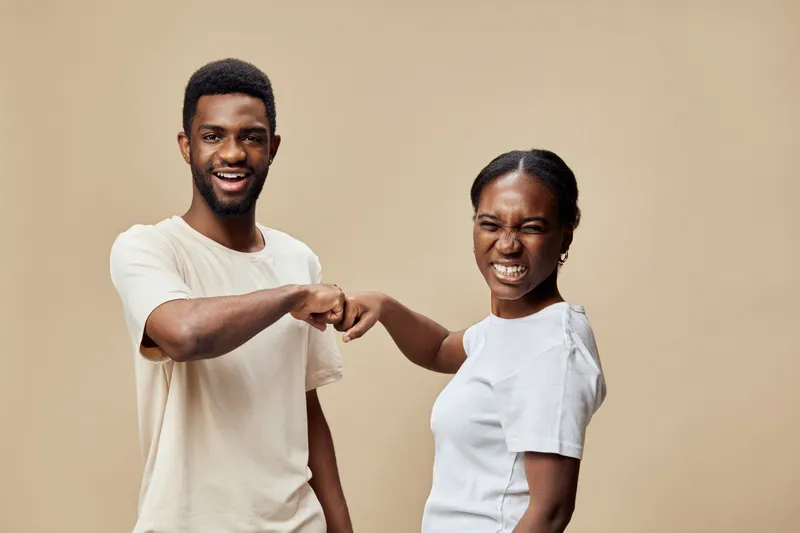 Happy diverse young couple smiling and fist bumping against a neutral background, exuding joy and connection, ideal for themes of love and unity