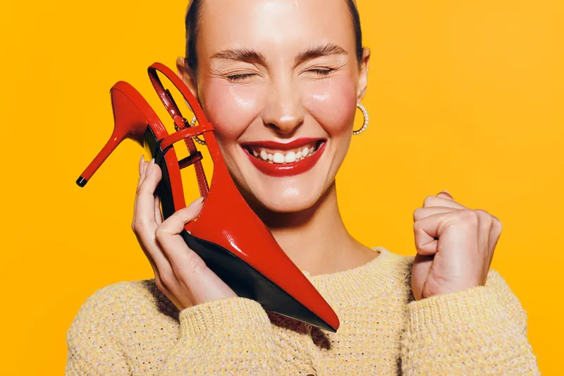 Happy woman with red high heel shoes smiles with closed eyes on yellow background. Concept of fashion, style, joy, and female confidence in bright studio lighting.