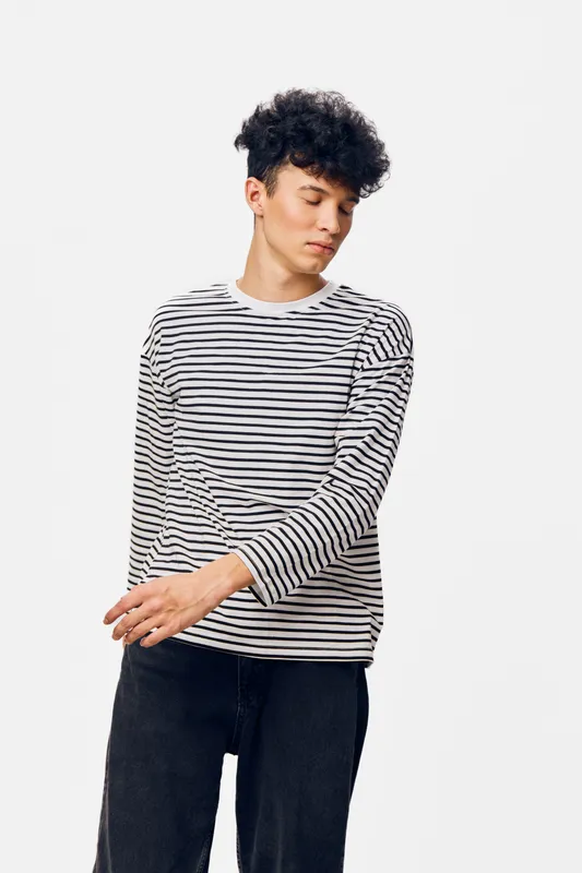 young man with curly hair wearing striped long sleeve shirt and black pants standing against white background, casual style, relaxed pose