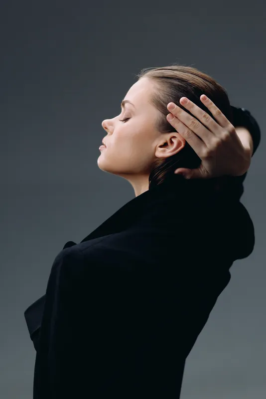 Calm woman with closed eyes in black coat expressing peacefulness and introspection on dark gray background