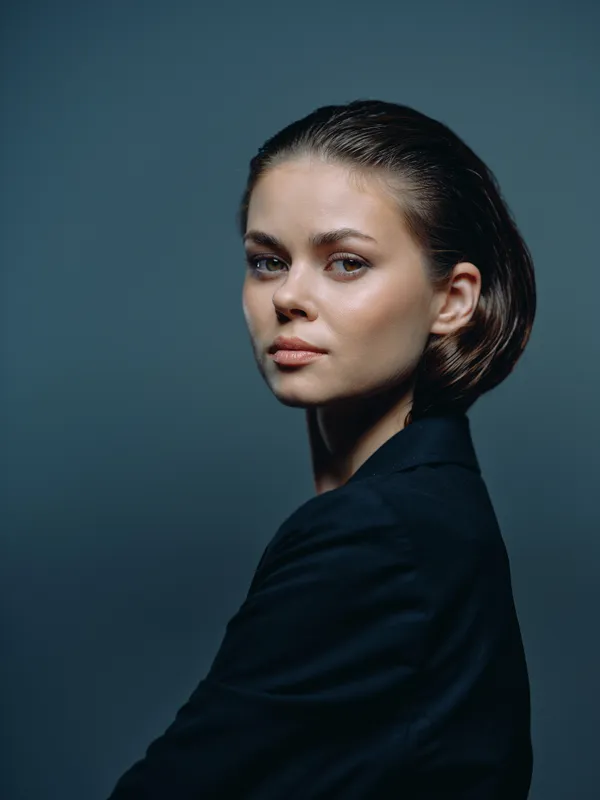 Portrait of a serious woman with slicked-back hair wearing a dark jacket in a studio setting