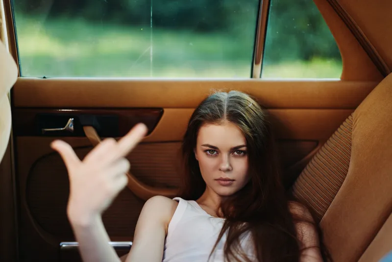 Defiant young woman in a car showing a rebellious attitude, showcasing confidence and strength with a bold expression.