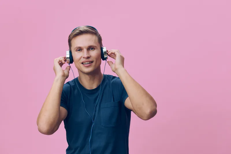 Man listening to music with headphones on a pink background, casual blue t-shirt, smiling, cheerful, relaxed, lifestyle concept, modern, youth, young adult, entertainment, leisure.