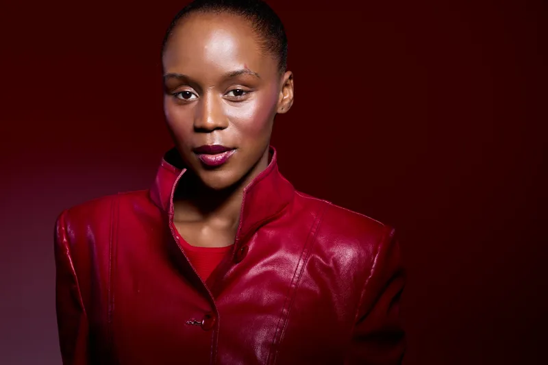 Portrait of confident dark skinned African woman wearing shiny red leather jacket against red background. Concept of fashion, beauty, elegance, and empowerment in studio lighting.