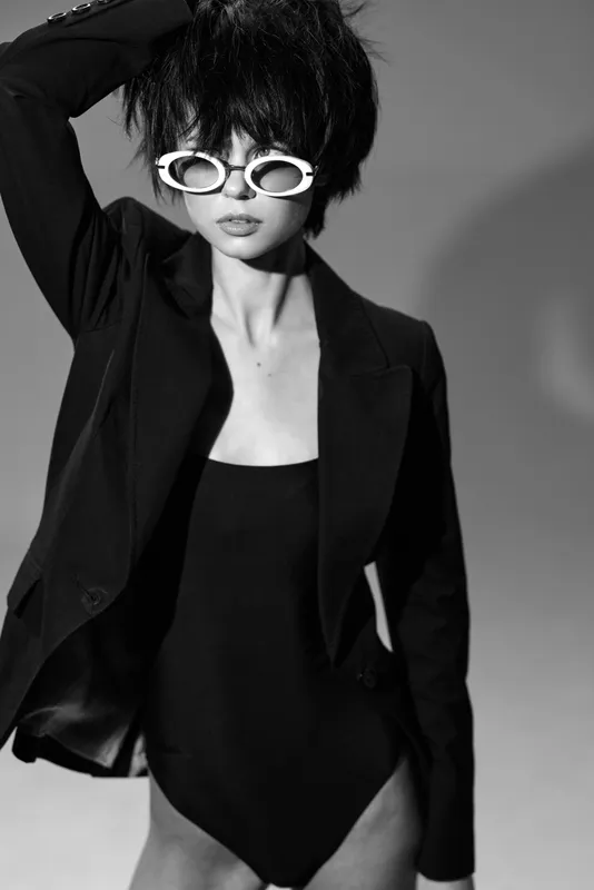 Black and white portrait of stylish woman wearing sunglasses and blazer with edgy hairstyle.