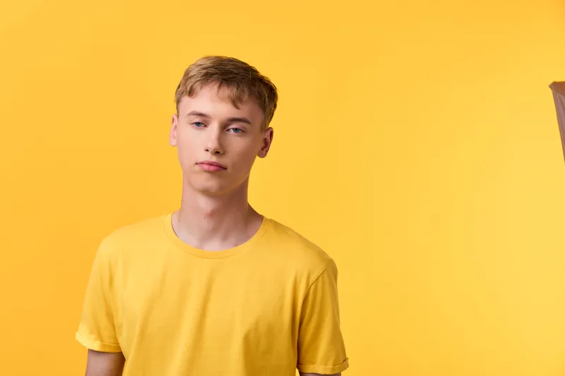 Young man in a yellow shirt against a yellow background captures casual style in a clean studio shot with minimal mood and bright color, evoking modern fashion photography and simplicity