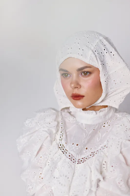 Elegant model in a white embroidered outfit displaying a contemplative expression against a soft, neutral background, showcasing seasonal fashion concepts